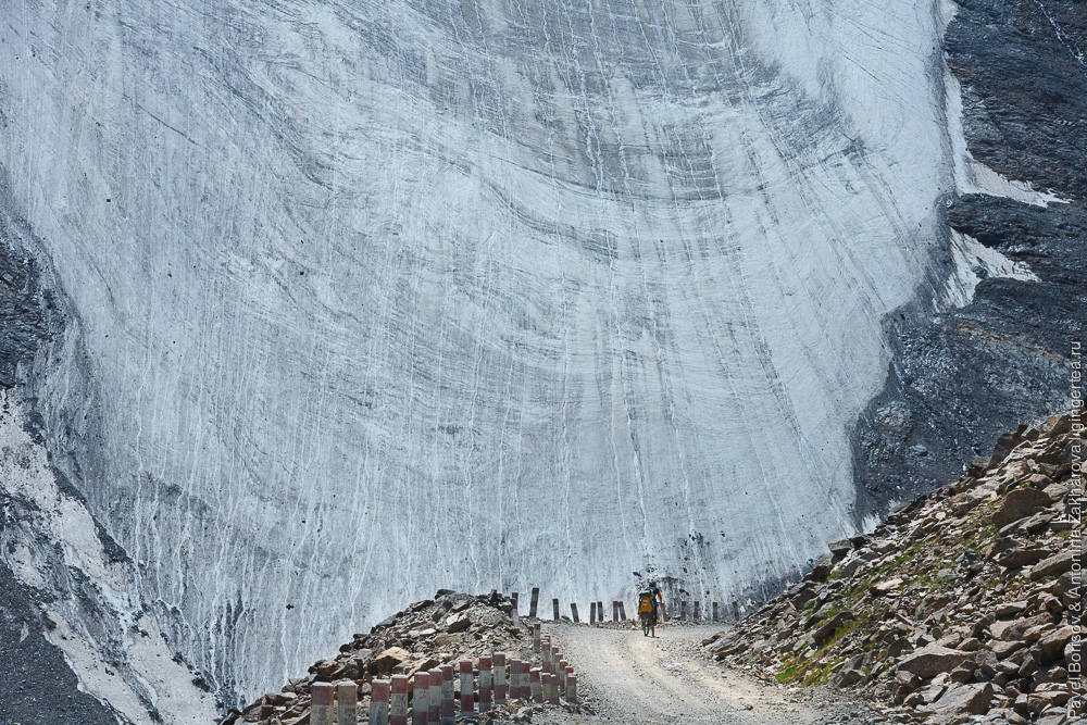 велосипедист едет по горной дороге на фоне ледника в Китайском Тянь-Шане