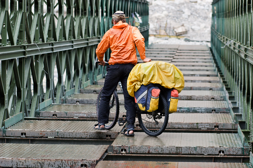 велосипедист идет по недостроенному мосту через реку Шайок в Ладакхе